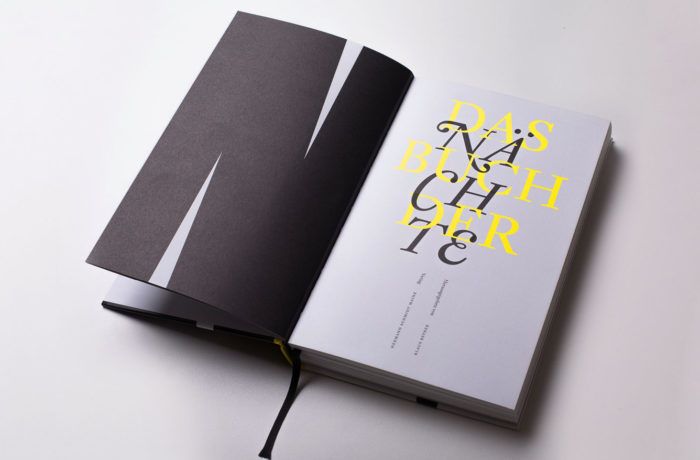 Ein aufgeschlagenes Buch mit schwarzem Einband zeigt eine Seite mit großen, sich überlappenden gelben und schwarzen Buchstaben, die in einer modernen, künstlerischen Schriftart auf hellgrauem Hintergrund die Worte „DAS BUCH DER NACHTE“ bilden.