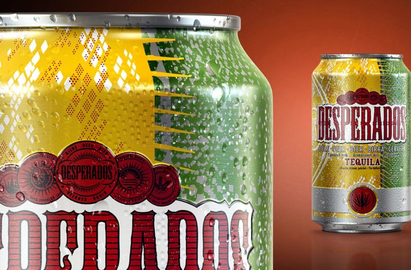 Nahaufnahme einer Desperados-Bierdose mit einem farbenfrohen, gelben, grünen und silbernen Design, mit roten Logos und Text. Eine weitere Desperados-Dose erscheint im Hintergrund auf einer rötlich-orangefarbenen Fläche mit Farbverlauf.