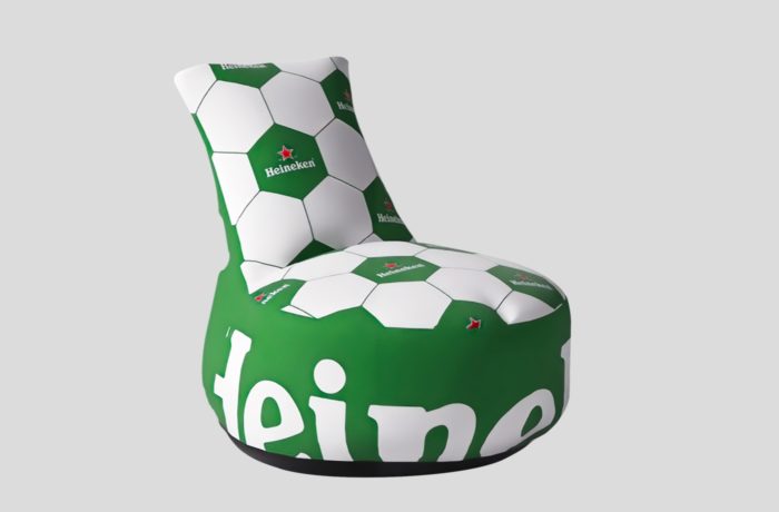 Ein moderner Stuhl mit einem grün-weißen Fußballmuster, auf dem das Heineken-Logo auf mehreren Feldern aufgedruckt ist, vor einem schlichten grauen Hintergrund.