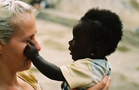Eine Frau hält ein Baby, das mit einer Hand sanft ihr Gesicht berührt. Die Frau, die das Baby lächelnd anschaut, genießt diesen süßen Moment im Freien - eine zärtliche Szene, die Madamfo Ghanas Geist der Fürsorge und Verbundenheit widerspiegelt.
