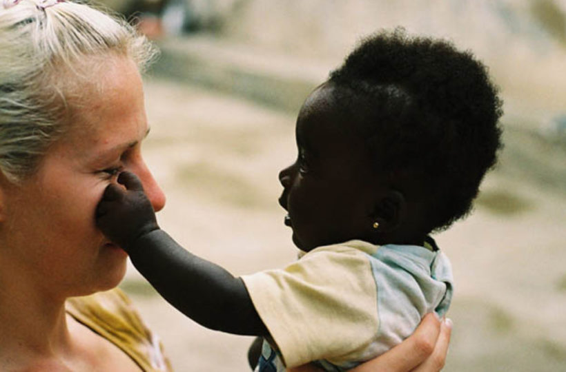 Eine Frau hält ein Baby, das mit einer Hand sanft ihr Gesicht berührt. Die Frau, die das Baby lächelnd anschaut, genießt diesen süßen Moment im Freien - eine zärtliche Szene, die Madamfo Ghanas Geist der Fürsorge und Verbundenheit widerspiegelt.