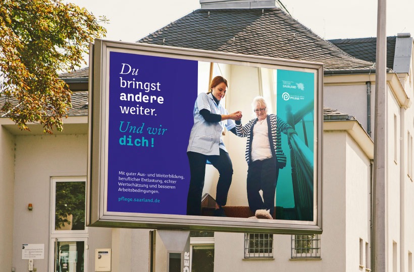 Ein Plakat zeigt eine Pflegekraft, die einer älteren Frau beim Gehen hilft. Der Text auf Deutsch lautet: Du bringst andere weiter. Und wir dich!" und wirbt für die Pflegearbeit und die Unterstützung durch das Gesundheitsministerium für Pflegekräfte im Saarland, Deutschland.