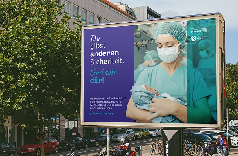 Ein Plakat zeigt eine Krankenschwester in Kittel, Maske und Mütze, die ein neugeborenes Baby hält. Der Text ist auf Deutsch und stammt vom Ministerium für Gesundheit, das für die Krankenpflege wirbt: Sie geben anderen Sicherheit. Und wir geben sie Ihnen! auf einer Straße in der Stadt.