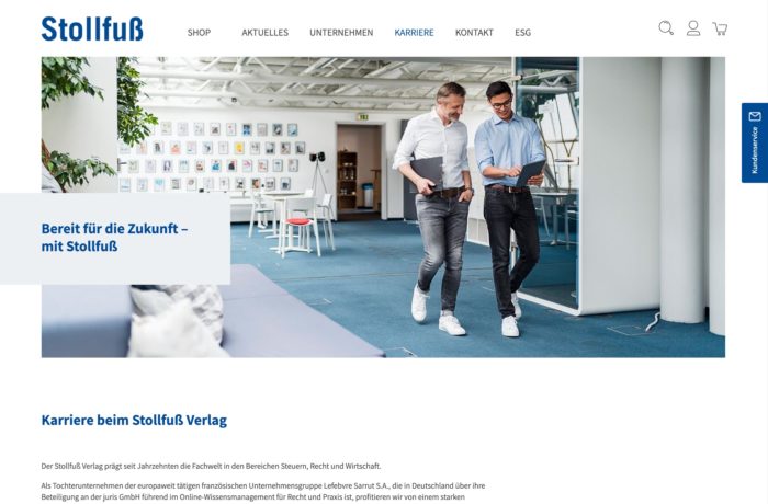 Zwei Männer gehen und unterhalten sich in einem modernen Büro mit weißen Schreibtischen, blauen Stühlen und großen Fenstern. Der Raum ist hell, an der Rückwand hängen Fotos. Auf einem blauen Transparent steht: Bereit für die Zukunft - mit Stollfuß. Zwei Männer gehen und unterhalten sich in einem modernen Büro mit weißen Schreibtischen, blauen Stühlen und großen Fenstern. Der Raum ist hell, an der Rückwand hängen Fotos. Auf einem blauen Transparent steht: Bereit für die Zukunft - mit Stollfuß.