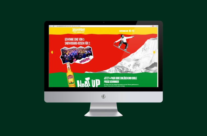 Ein Computermonitor zeigt eine farbenfrohe Website mit einem springenden Snowboarder, einer Getränkeflasche und einem Werbetext in deutscher Sprache mit einem Berg im Hintergrund. Das Design verwendet rote, gelbe und grüne Abschnitte.
