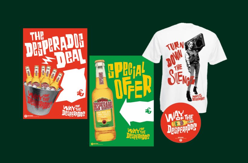 Ein Werbedisplay zeigt Desperados-Plakate, ein T-Shirt mit einer Person, die einen Ghettoblaster trägt, eine Flasche mit dem Text "Special Offer" und einen runden Untersetzer, alle mit lebendigen Grafiken auf dunkelgrünem Hintergrund.
