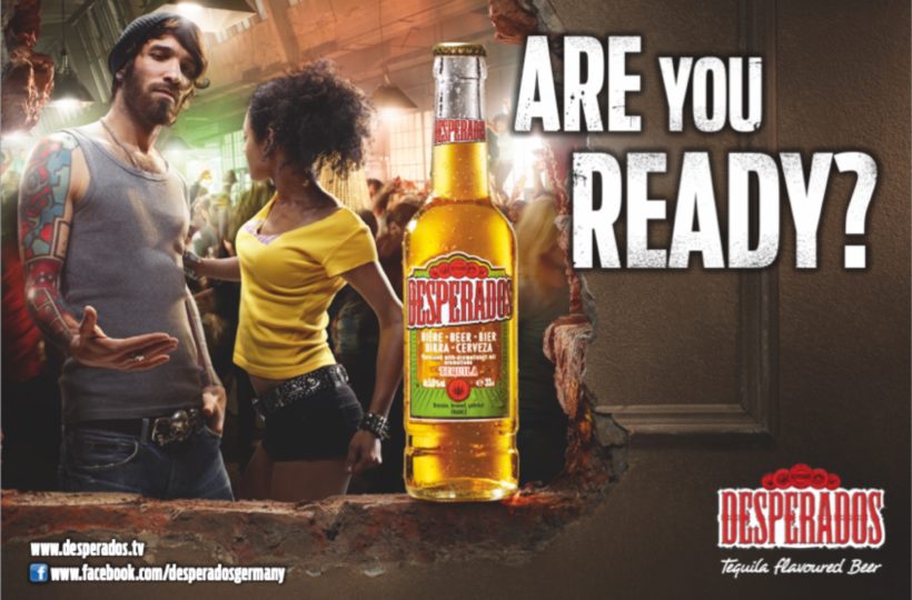 In der Mitte ist eine Desperados-Bierflasche zu sehen, auf der ein tätowierter Mann und eine Frau auf einer ausgelassenen Party tanzen. Der große Text lautet ARE YOU READY? und das Desperados-Branding erscheint unten.